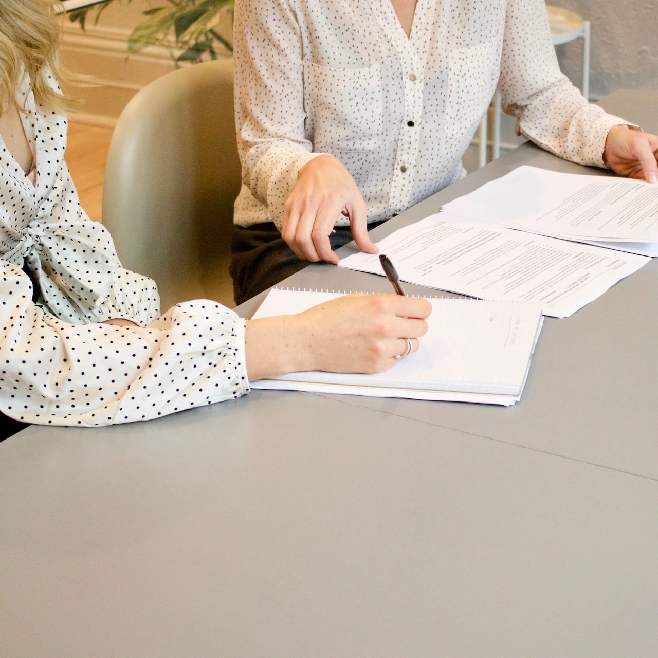 woman signing on white printer paper beside woman about to touch the documents
